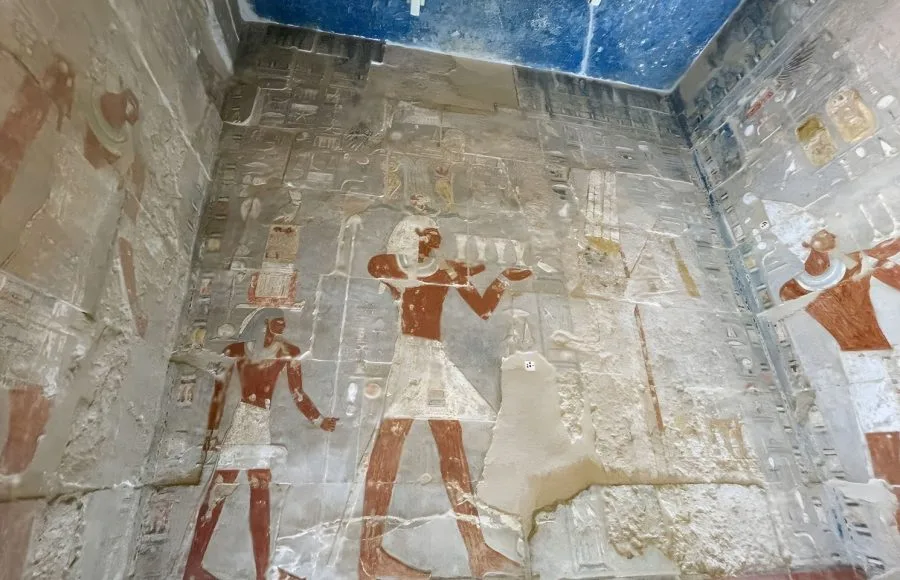 A detailed view of the colorful, well-preserved tomb paintings and hieroglyphs on a wall inside a tomb within the Valley of the Kings Luxor.