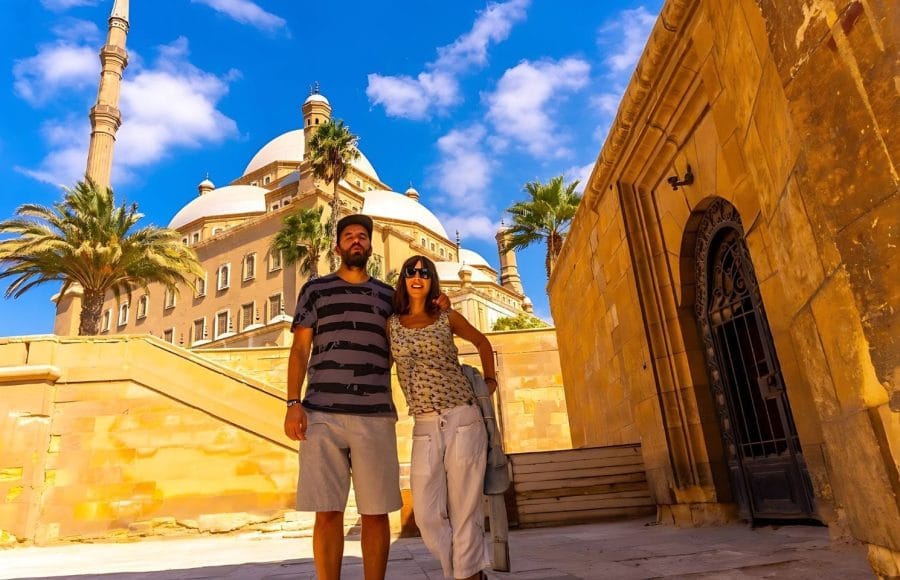 A couple of tourists smiling at the camera in front of the Mosque of Muhammad Ali Pasha at the Citadel of Cairo.