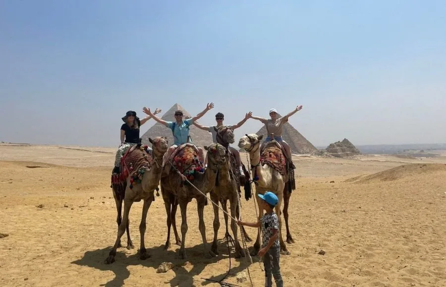 Tourists enjoying a camel ride adventure with a guide near the Great Pyramids of Giza Egypt