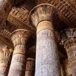 An upward view of the Colorful Columns of the Ancient Khnum Temple in Esna, showing the magnificent original colors and detailed hieroglyphic reliefs on the columns and ceiling.