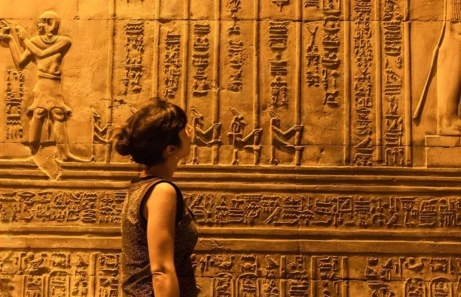 A woman closely examining the detailed hieroglyphic carvings on a wall inside the Kom Ombo Temple.
