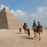 Tourists riding camels across the plateau of the Great Pyramids of Giza.