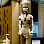 A colossal, ancient Egyptian statue of Pharaoh Ramses II, standing tall in the modern, soaring atrium Inside Gem Grand Egyptian Museum (GEM) in Giza.