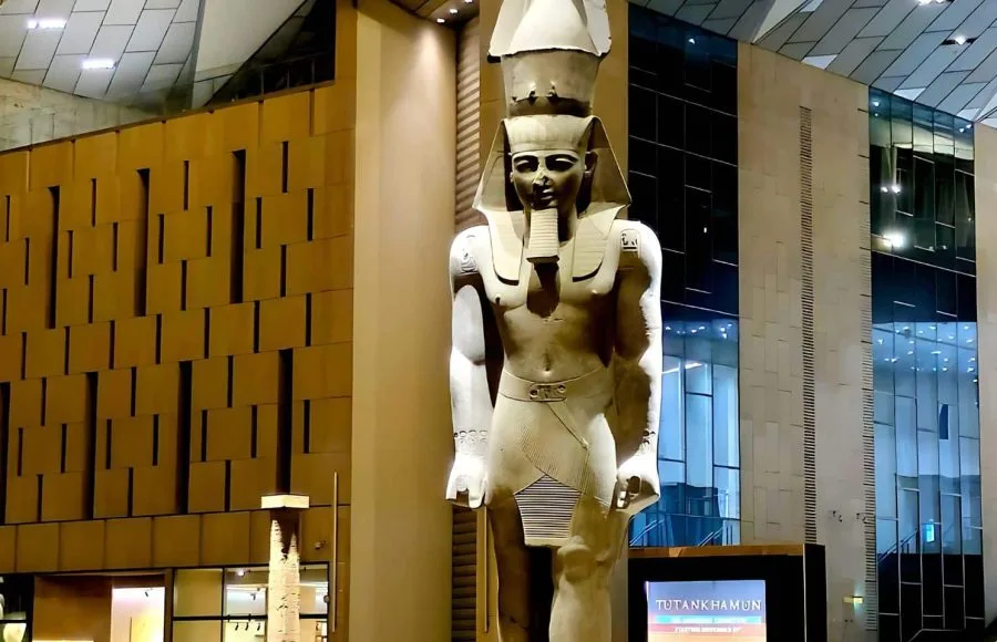 A colossal, ancient Egyptian statue of Pharaoh Ramses II, standing tall in the modern, soaring atrium Inside Gem Grand Egyptian Museum (GEM) in Giza.