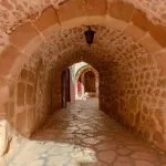 An interior view of Inside St Catherine's Monastery Sinai, showing a stone-paved arched hallway with rough stone walls, leading to another arched passage deeper within the ancient structure.