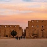 The massive stone entrance pylon of the Karnak Temple complex at Sunset in Luxor, Egypt, with the sky glowing in shades of orange and pink.