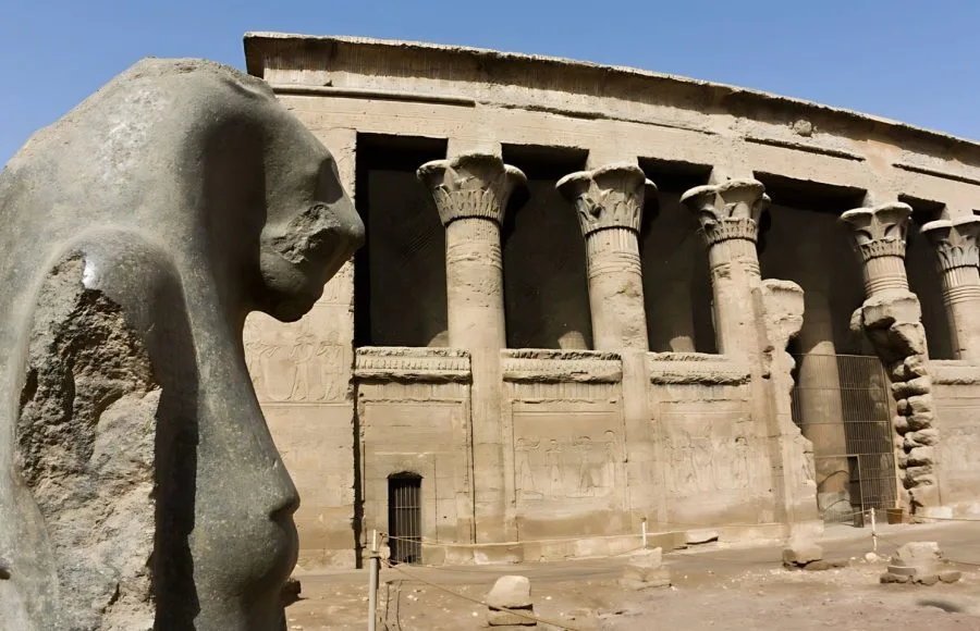 The well-preserved hypostyle hall of Khnum Temple at Esna Egypt, featuring large Ptolemaic columns with detailed capitals and a broken statue in the foreground.