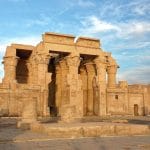 The ancient Kom Ombo Temple is seen from the Nile River at sunset, with its columns and walls.