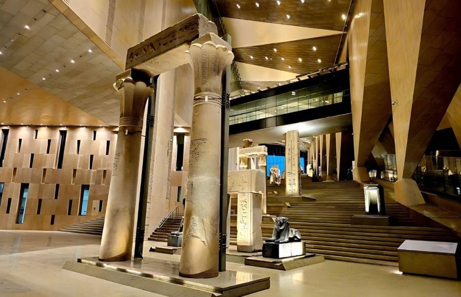 Interior view of the Grand Egyptian Museum (GEM) featuring massive stone lotus columns and ancient monuments in a modern hall.