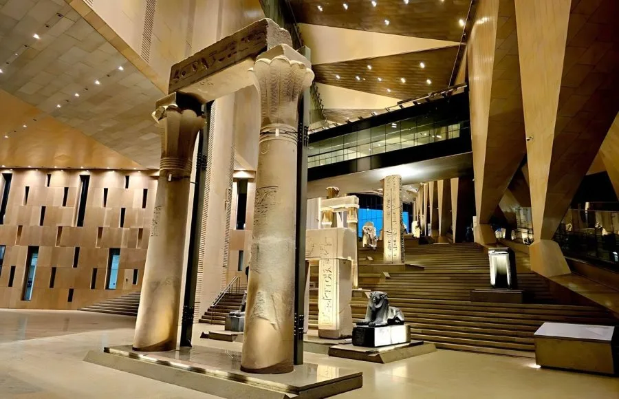 Interior view of the Grand Egyptian Museum (GEM) featuring massive stone lotus columns and ancient monuments in a modern hall.