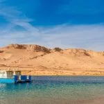 A small boat resting on clear, water with a vast desert mountain.