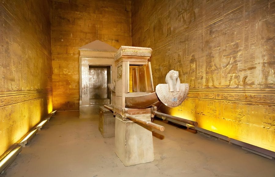 A view of the beautifully preserved ritual barque and shrine, including a white falcon statue, inside The Sanctuary Inside Temple of Edfu Egypt, illuminated by warm golden light.