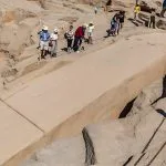 Tourists walking around the Unfinished Obelisk in Aswan, a massive stone carving still attached to its quarry.