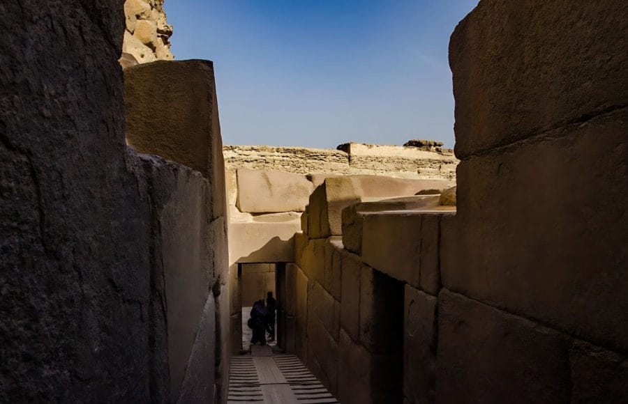A dark, narrow passageway framed by colossal stone blocks leads into The Valley of Khafre Temple at the Giza Plateau.