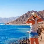 A tourist standing on a cliff, looking out over the blue Sea at Dahab .