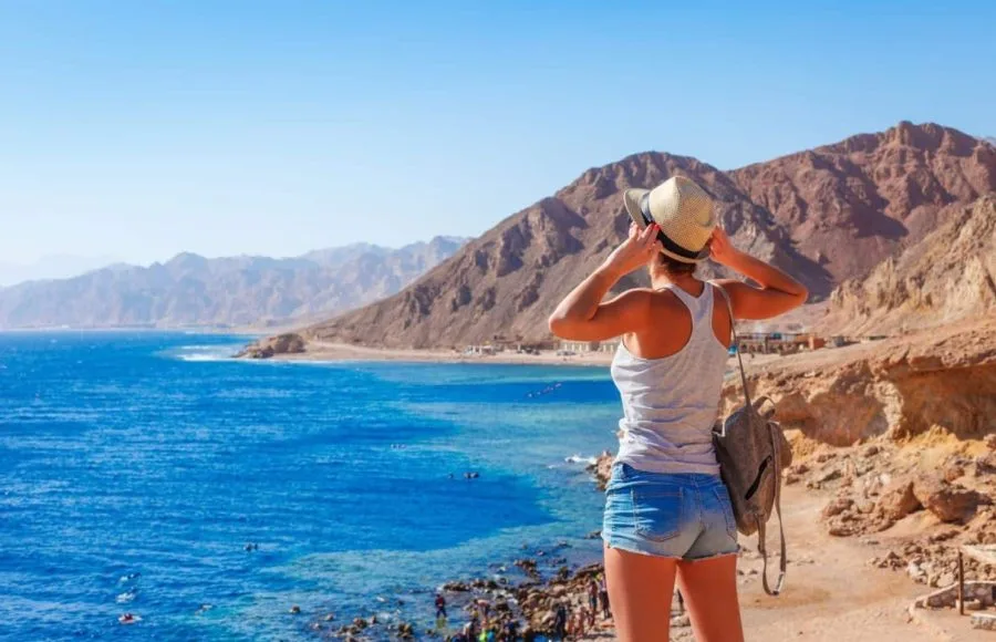 A tourist standing on a cliff, looking out over the blue Sea at Dahab .
