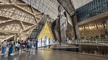 Tourists viewing the colossal statue in the stunning, sunlit atrium of the new Grand Egyptian Museum in Giza.