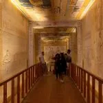 Tourists walking through a long, illuminated hallway with ancient hieroglyphics carved into the walls, a common sight at the Valley of the Kings.