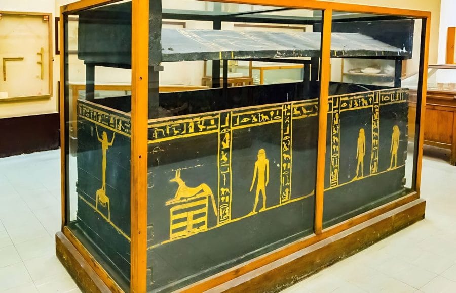 A black granite Valley Of The Kings granet Coffin displayed in a museum, intricately decorated with golden yellow hieroglyphs and scenes, originally from the tombs in the Valley of the Kings.