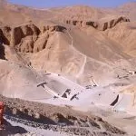A tourist looking at the Valley of the Kings desert landscape in Luxor, showing tomb entrances.