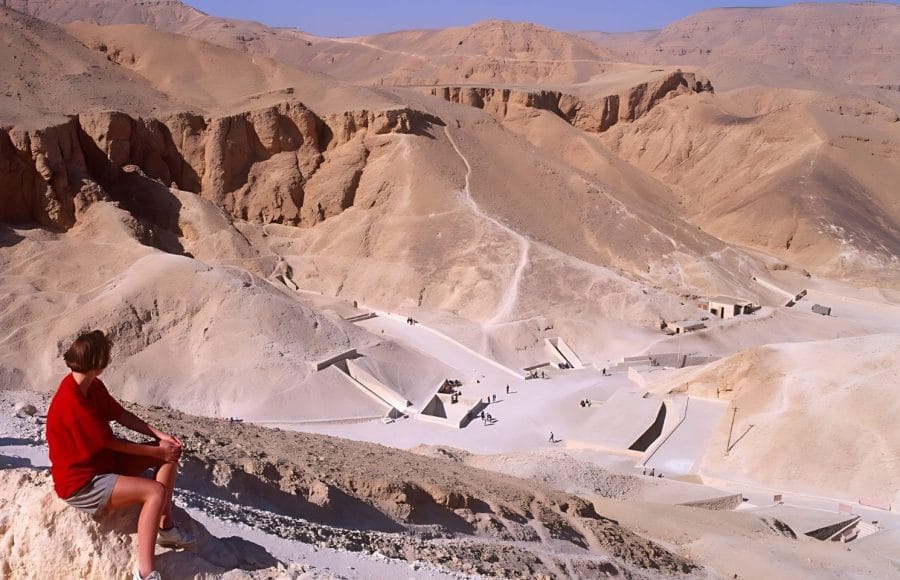 A tourist looking at the Valley of the Kings desert landscape in Luxor, showing tomb entrances.