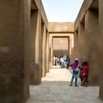 Tourists walk through the imposing corridor lined with massive aswan granite pillars within the valley temple of khafre at Giza.