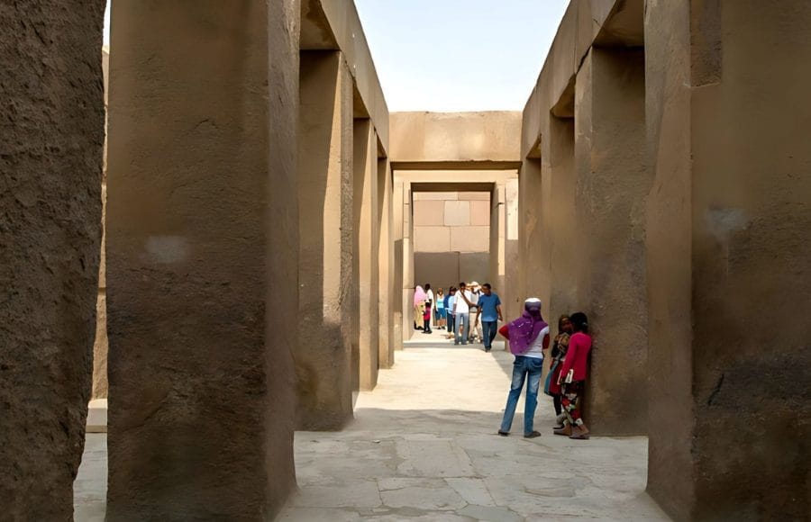 Tourists walk through the imposing corridor lined with massive aswan granite pillars within the valley temple of khafre at Giza.