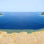 Panoramic view of the Blue Hole, a renowned diving and snorkeling site, showing the deep blue water and surrounding desert cliffs..