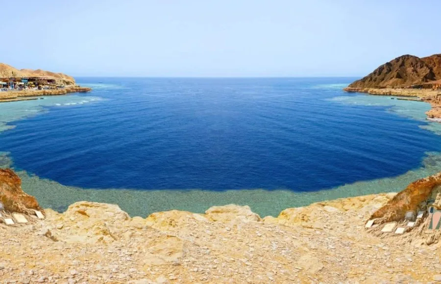 Panoramic view of the Blue Hole, a renowned diving and snorkeling site, showing the deep blue water and surrounding desert cliffs..
