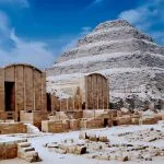 A wide view of the ancient, weathered stone blocks and surrounding ruins of the Saqqara Step Pyramid of King Djoser, the earliest monumental structure in Egypt.
