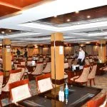 The elegant dining room of the Blue Shadow i Nile Cruise, featuring numerous tables set with white tablecloths and comfortable chairs.