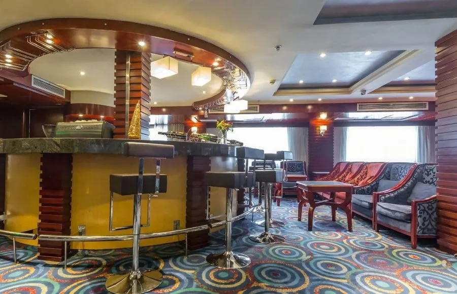 A stylish lounge bar on the Blue Shadow i Nile Cruise, with comfortable seating, a well-stocked bar, and a large window overlooking the river.