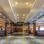 The main lounge of the Blue Shadow i Nile Cruise, showing a spacious seating area with large windows, comfortable sofas, and a television.