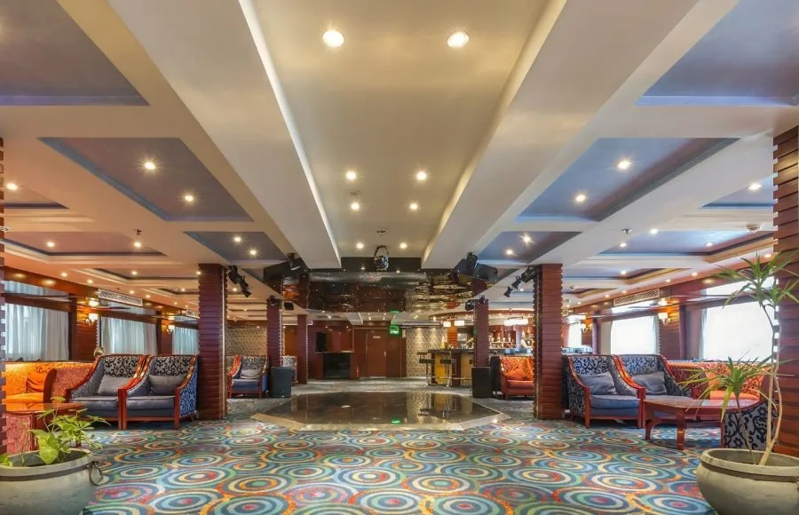 The main lounge of the Blue Shadow i Nile Cruise, showing a spacious seating area with large windows, comfortable sofas, and a television.