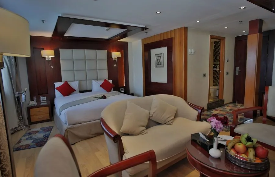 The luxurious suite on the Blue Shadow i Nile Cruise, featuring a comfortable king-size bed, a separate seating area, and a large window with a scenic view.