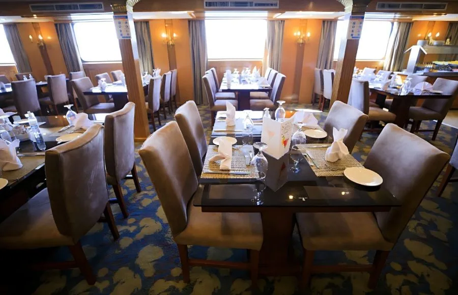Dining area of the Blue Shadow iii Nile Cruise, with tables set for guests and large windows offering views of the river.