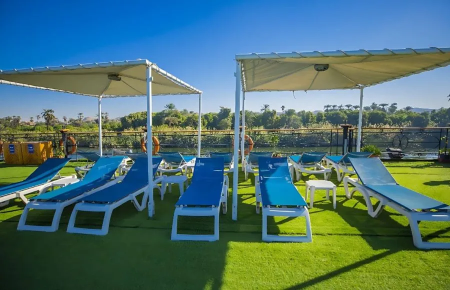 The sun deck of the Ms Blue Shadow iii Nile Cruise, showing rows of blue lounge chairs and white umbrellas on an artificial grass surface.