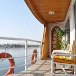 A captivating view of the Nile River from the private balcony of a cabin aboard the luxurious HS Solaris I Nile Cruise, featuring comfortable chairs and a lifebuoy.