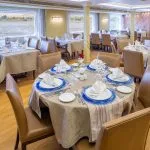 A beautifully set dining room on the HS Solaris I Nile Cruise, with tables arranged for guests and large windows offering panoramic views of the Nile River.