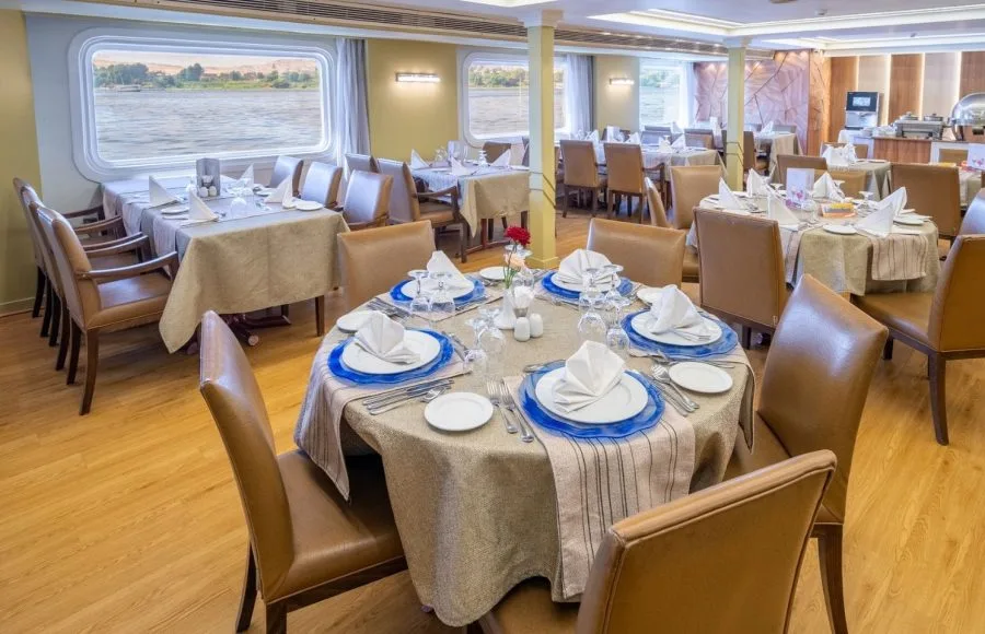 A beautifully set dining room on the HS Solaris I Nile Cruise, with tables arranged for guests and large windows offering panoramic views of the Nile River.