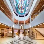 The stunning multi-level lobby of the HS Solaris I Nile Cruise, featuring a beautiful stained-glass ceiling, elegant staircase, and a view of the river.