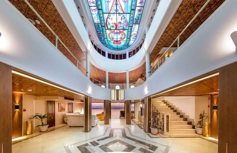 The stunning multi-level lobby of the HS Solaris I Nile Cruise, featuring a beautiful stained-glass ceiling, elegant staircase, and a view of the river.