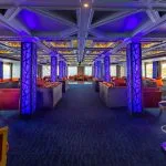 The vibrant lounge area of the HS Solaris I Nile Cruise, illuminated with striking blue and purple lighting, offering comfortable seating and panoramic river views.