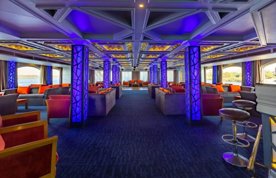 The vibrant lounge area of the HS Solaris I Nile Cruise, illuminated with striking blue and purple lighting, offering comfortable seating and panoramic river views.