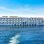 The impressive HS Solaris I Nile Cruise ship moving gracefully on the sparkling waters of the Nile River under a clear blue sky.