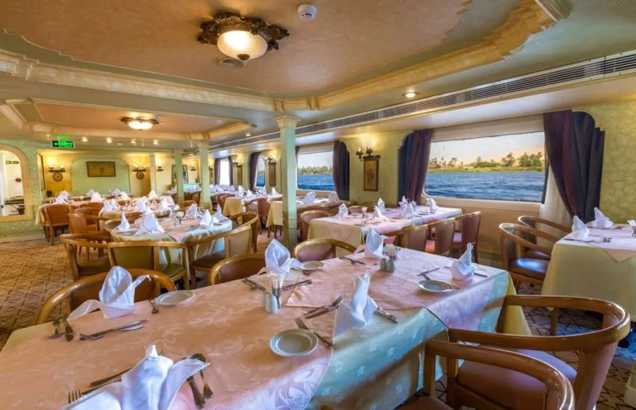 An elegantly set dining room on the HS Solaris I Nile Cruise, featuring beautifully prepared tables and large windows offering scenic views of the Nile River.