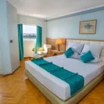 A bright and comfortable cabin on the HS Solaris I Nile Cruise, featuring a cozy bed, seating area, and a balcony door offering stunning views of the Nile River.