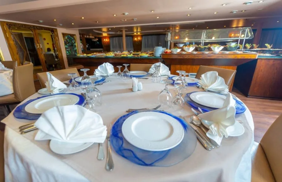 An elegant restaurant and buffet area on the Solaris II Nile Cruise, featuring a beautifully set dining table with fine cutlery and glassware