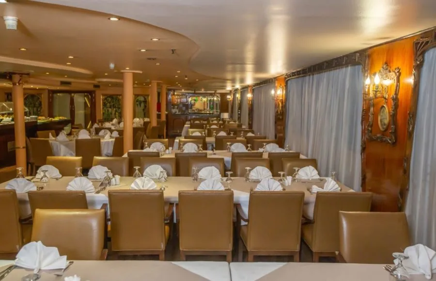 The elegant and spacious restaurant on the Solaris 2 Nile cruise, featuring multiple dining tables with comfortable seating and a buffet in the background