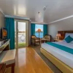 The luxurious single cabin on the Solaris II Nile Cruise, featuring a king-sized bed, a seating area, and a balcony with a stunning view of the Nile River